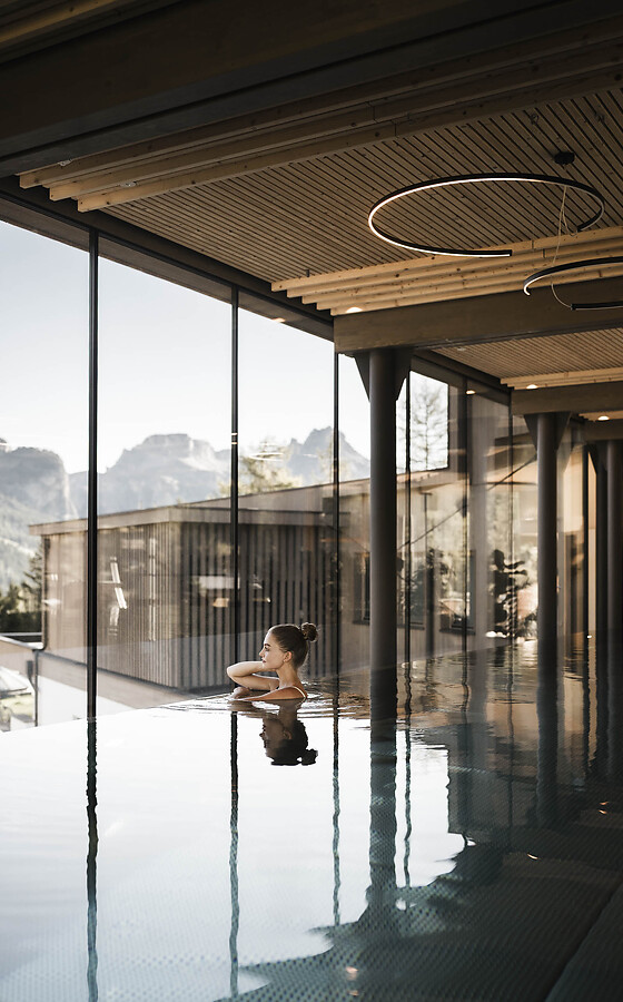 Woman in the light-filled indoor pool with a modern wooden ceiling and large windows overlooking the mountain landscape.