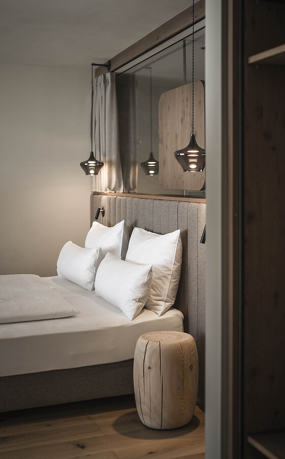 Double bed with white pillows, an upholstered headboard and decorative pendant lights in a hotel room.